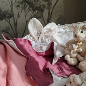 Doudou plat lapin Myrtille en gaze de coton framboise posé dans un berceau pour bébé - Cœur de Pinpin